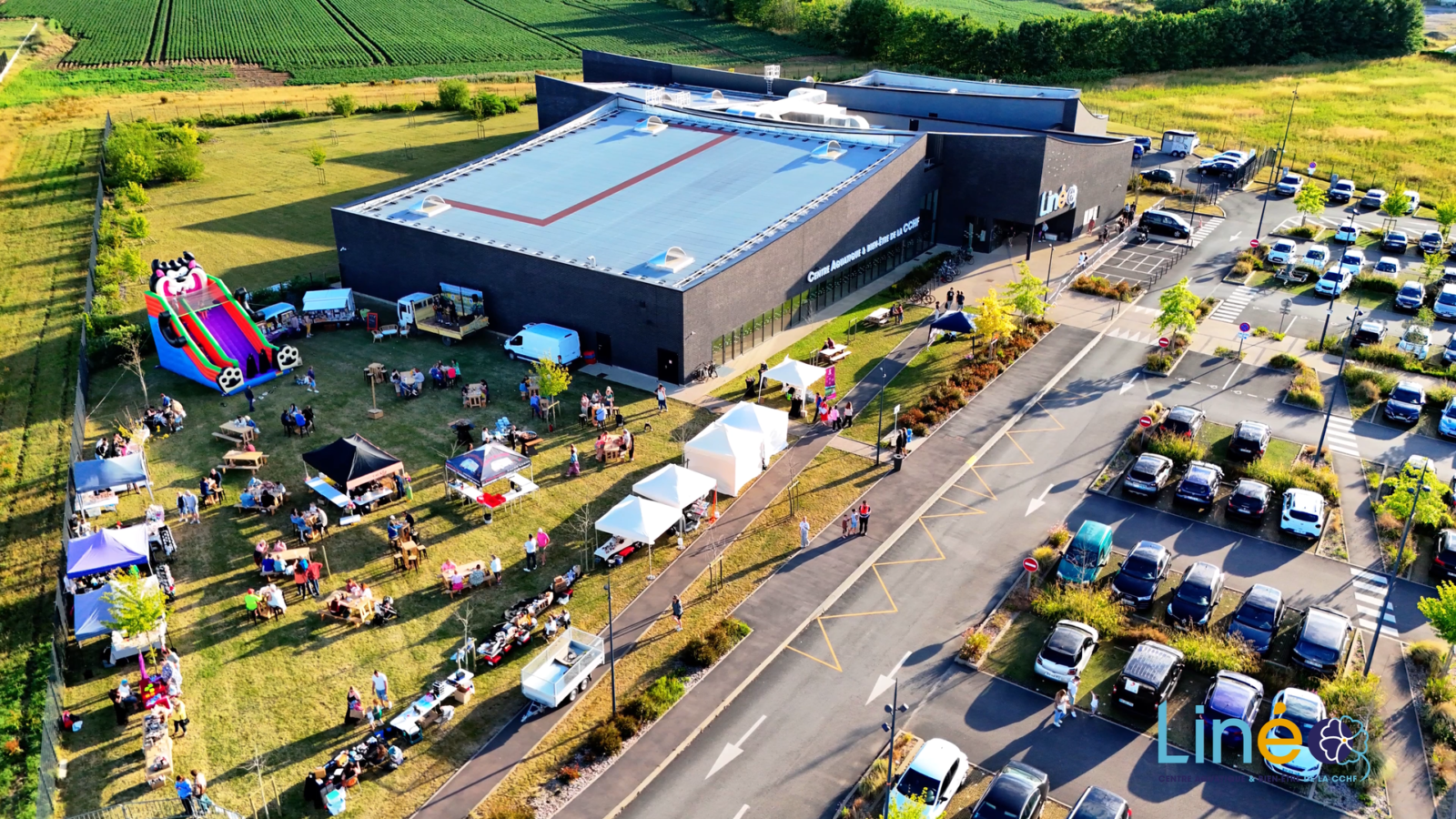 Centre aquatique Linéo à Wormhout vu par drone pendant la pool party : pelouse avec stands, tables, structure gonflable et public