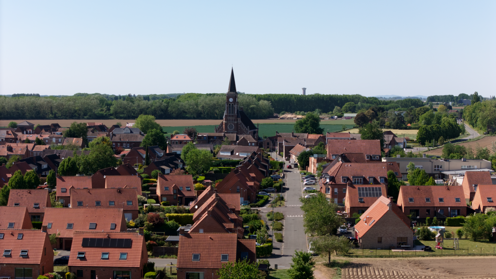 Vue aérienne de Marquillies par drone : maisons de brique, rue menant à l'église Sainte-Geneviève et campagne des Weppes, mai 2025